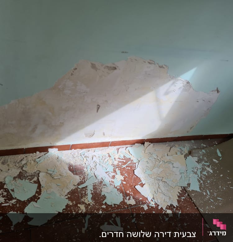 קיר עם צבע מתקלף וחתיכות צבע על הרצפה